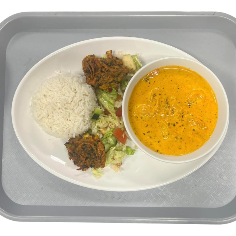 Indian meal with rice, pakoras, salad, and a bowl of orange curry on a white plate.