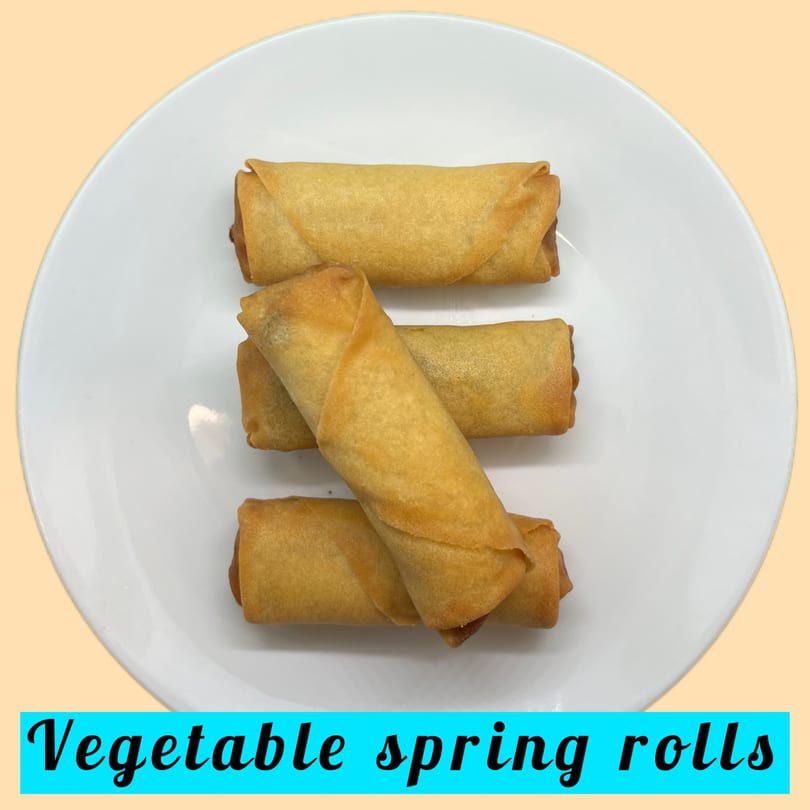 Four golden-brown vegetable spring rolls arranged on a white plate, viewed from above.