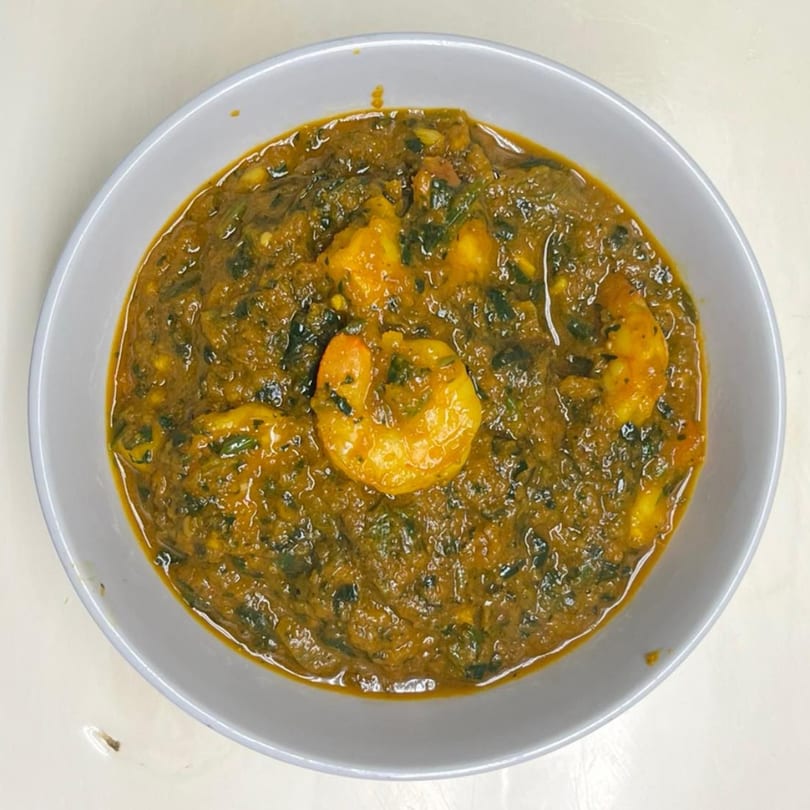 A close-up of a bowl of Indian shrimp curry with a rich, dark green sauce.