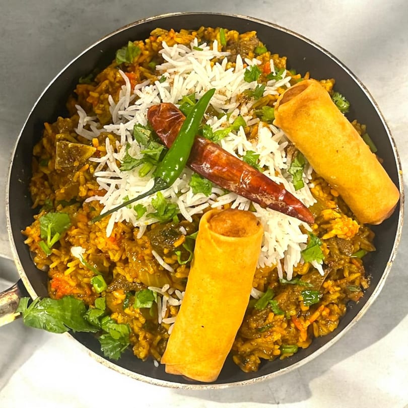 Indian biryani with rice, green chilies, dried red chilies, cilantro, and two spring rolls.