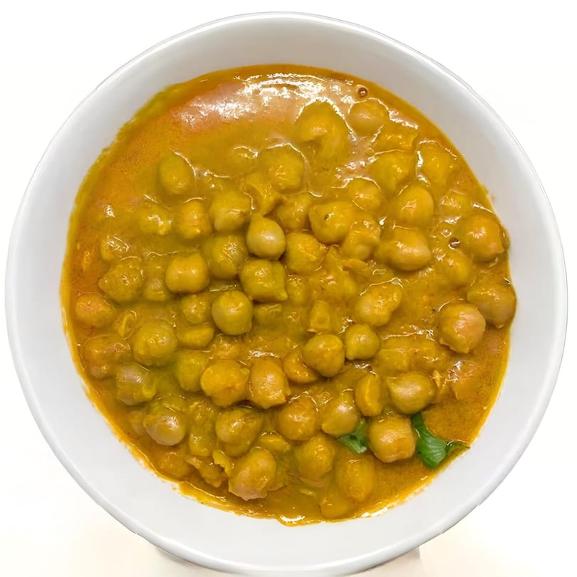 A white bowl filled with Indian chana masala, featuring chickpeas in a rich, golden-orange curry sauce.
