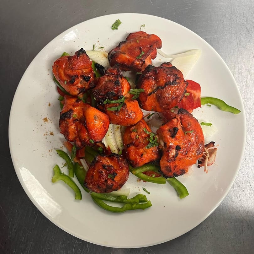 Indian chicken tikka, garnished with green peppers, onions, and herbs, on a white plate.