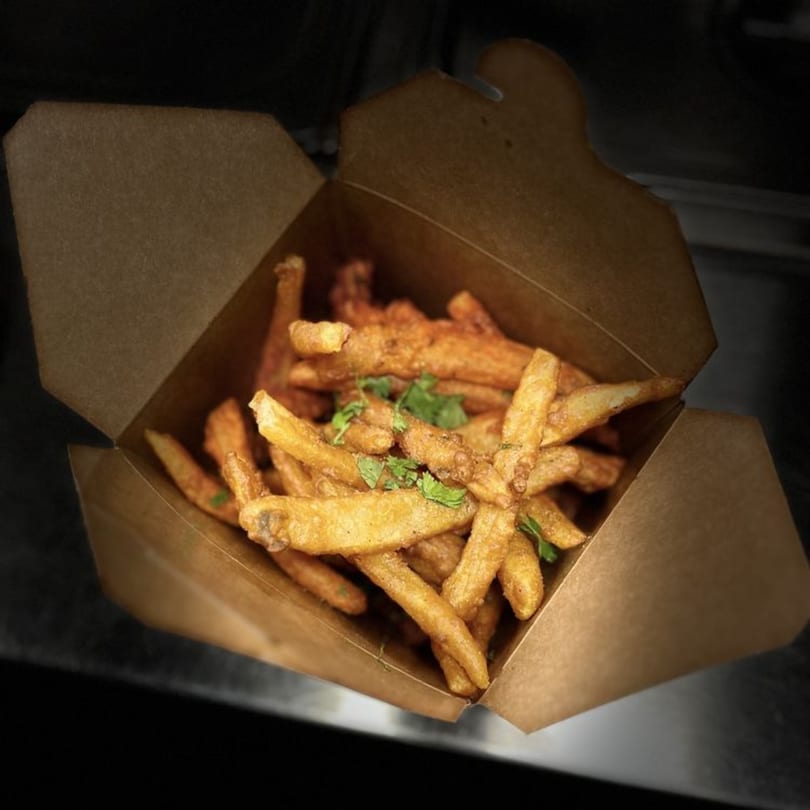 Crispy golden Indian-spiced fries in a brown takeout box, garnished with fresh cilantro.
