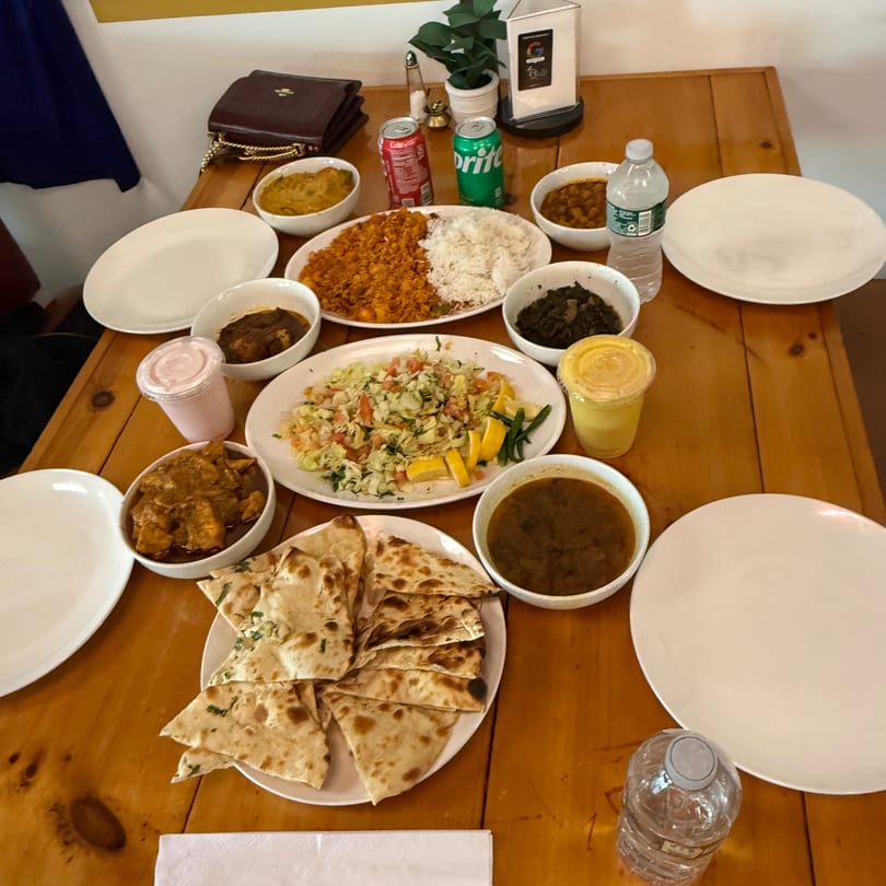 A wooden table laden with various Indian dishes, including rice, curries, naan, and drinks.