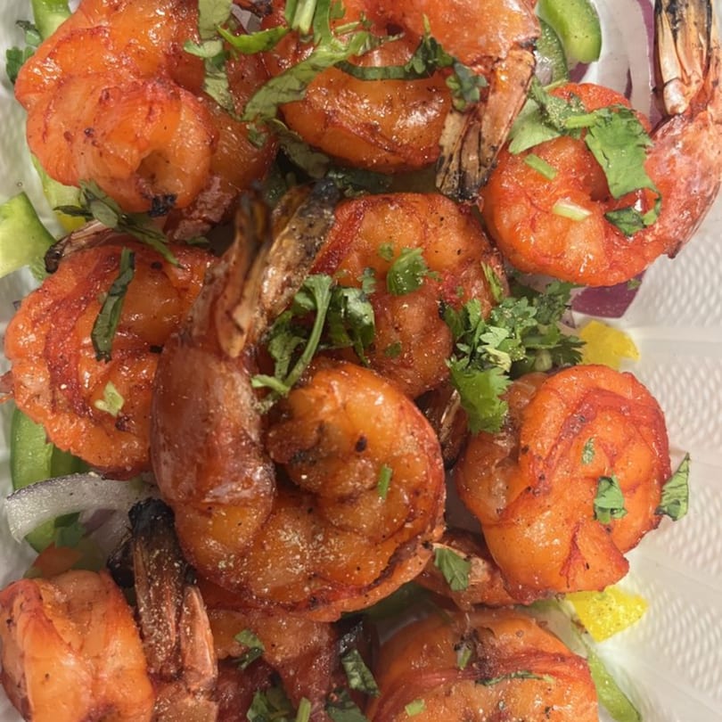 Close-up of vibrant orange Indian shrimp, garnished with fresh green herbs and spices.